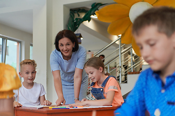 Image showing Creative kids during an art class in a daycare center or elementary school classroom drawing with female teacher.