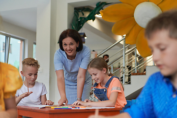 Image showing Creative kids during an art class in a daycare center or elementary school classroom drawing with female teacher.