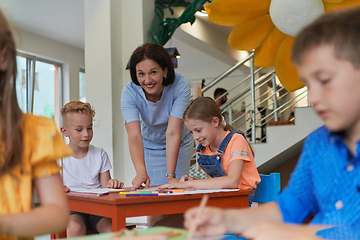 Image showing Creative kids during an art class in a daycare center or elementary school classroom drawing with female teacher.