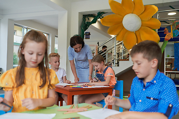 Image showing Creative kids during an art class in a daycare center or elementary school classroom drawing with female teacher.