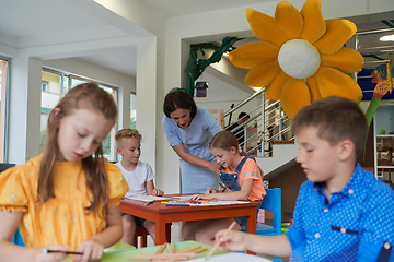 Image showing Creative kids during an art class in a daycare center or elementary school classroom drawing with female teacher.