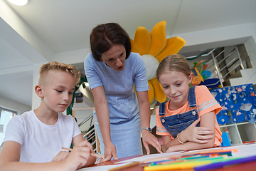 Image showing Creative kids during an art class in a daycare center or elementary school classroom drawing with female teacher.