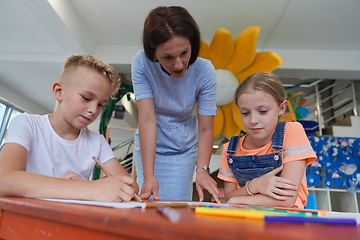 Image showing Creative kids during an art class in a daycare center or elementary school classroom drawing with female teacher.