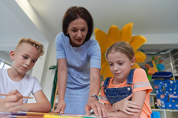 Image showing Creative kids during an art class in a daycare center or elementary school classroom drawing with female teacher.