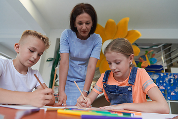 Image showing Creative kids during an art class in a daycare center or elementary school classroom drawing with female teacher.