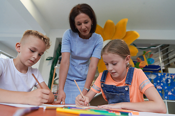 Image showing Creative kids during an art class in a daycare center or elementary school classroom drawing with female teacher.