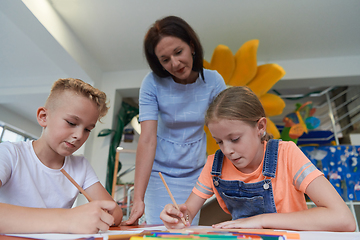 Image showing Creative kids during an art class in a daycare center or elementary school classroom drawing with female teacher.