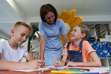 Image showing Creative kids during an art class in a daycare center or elementary school classroom drawing with female teacher.