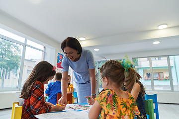 Image showing Creative kids during an art class in a daycare center or elementary school classroom drawing with female teacher.