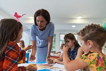 Image showing Creative kids during an art class in a daycare center or elementary school classroom drawing with female teacher.