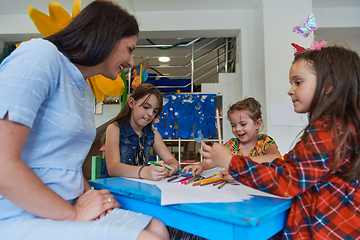 Image showing Creative kids during an art class in a daycare center or elementary school classroom drawing with female teacher.