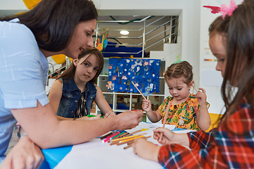 Image showing Creative kids during an art class in a daycare center or elementary school classroom drawing with female teacher.