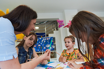 Image showing Creative kids during an art class in a daycare center or elementary school classroom drawing with female teacher.