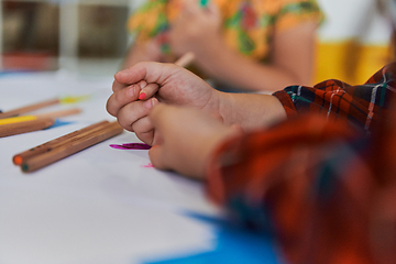 Image showing Close up photo of kids during an art class in a daycare center or elementary school classroom drawing with female teacher.