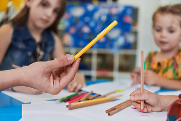 Image showing Close up photo of kids during an art class in a daycare center or elementary school classroom drawing with female teacher.