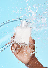 Image showing Water splash, black man and hand with skincare bottle in studio on a blue background. Hygiene, cleaning and male model holding lotion cosmetics or moisturizer product for beauty or skin health.