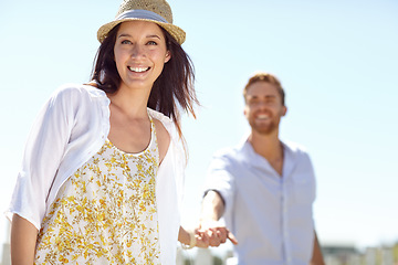 Image showing Young couple holding hands with smile for summer vacation, travel or journey together in the outdoors. Portrait of beautiful woman leading her boyfriend by the hand on a sunny day for the holiday