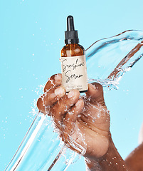 Image showing Serum, skincare and hand of a man with a water splash for an anti aging product, beauty and hair growth secret on a blue background in studio. Cosmetic, marketing and model with an oil for acne