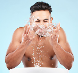 Image showing Face, water splash and skincare of man cleaning in studio isolated on a blue background. Hygiene, water drops and male model washing, bathing or grooming for healthy skin, facial wellness or beauty.