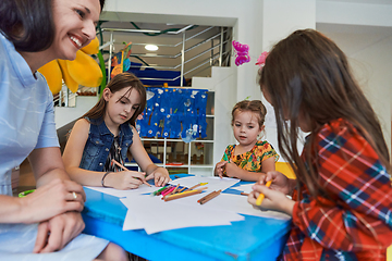 Image showing Creative kids during an art class in a daycare center or elementary school classroom drawing with female teacher.