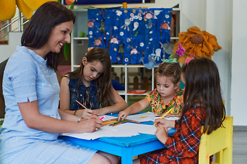 Image showing Creative kids during an art class in a daycare center or elementary school classroom drawing with female teacher.