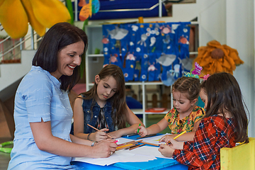 Image showing Creative kids during an art class in a daycare center or elementary school classroom drawing with female teacher.