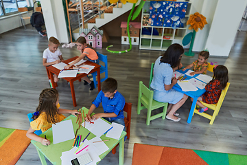 Image showing Creative kids during an art class in a daycare center or elementary school classroom drawing with female teacher.