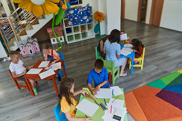 Image showing Creative kids during an art class in a daycare center or elementary school classroom drawing with female teacher.