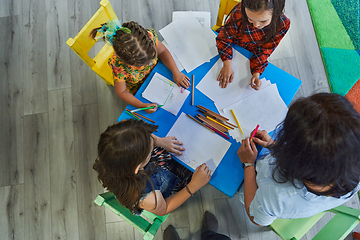 Image showing Creative kids during an art class in a daycare center or elementary school classroom drawing with female teacher.