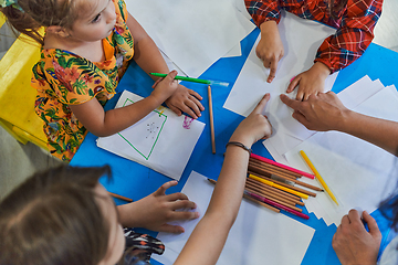 Image showing Creative kids during an art class in a daycare center or elementary school classroom drawing with female teacher.