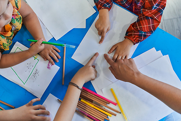 Image showing Creative kids during an art class in a daycare center or elementary school classroom drawing with female teacher.