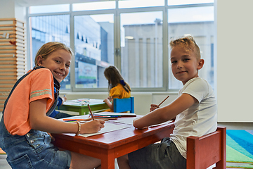 Image showing Cute girl and boy sit and draw together in preschool institution