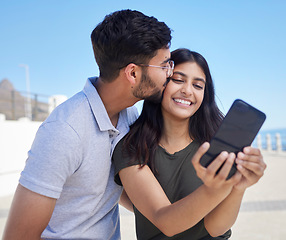 Image showing Phone, selfie and smile with couple at beach, travel and kiss by ocean with support, trust and outdoor for adventure in Mumbai. Smile in picture, happy memory with smartphone photography and romance