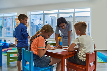 Image showing Creative kids during an art class in a daycare center or elementary school classroom drawing with female teacher.