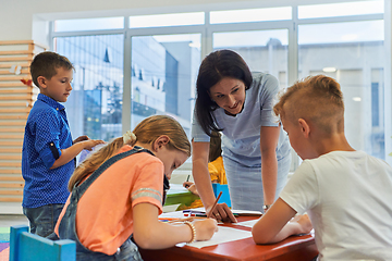 Image showing Creative kids during an art class in a daycare center or elementary school classroom drawing with female teacher.