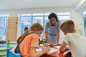 Image showing Creative kids during an art class in a daycare center or elementary school classroom drawing with female teacher.