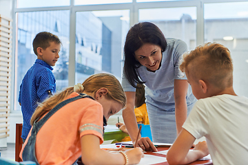 Image showing Creative kids during an art class in a daycare center or elementary school classroom drawing with female teacher.