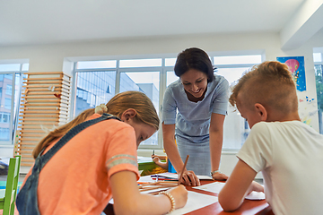 Image showing Creative kids during an art class in a daycare center or elementary school classroom drawing with female teacher.