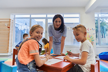 Image showing Creative kids during an art class in a daycare center or elementary school classroom drawing with female teacher.