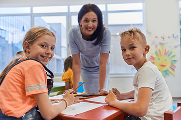 Image showing Creative kids during an art class in a daycare center or elementary school classroom drawing with female teacher.