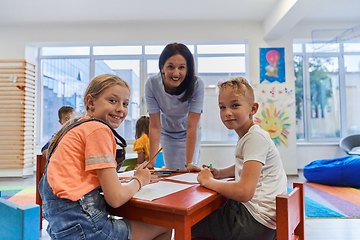 Image showing Creative kids during an art class in a daycare center or elementary school classroom drawing with female teacher.