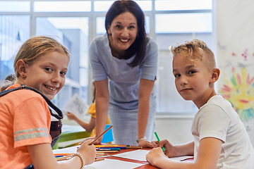 Image showing Creative kids during an art class in a daycare center or elementary school classroom drawing with female teacher.