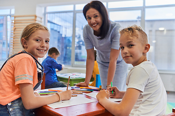 Image showing Creative kids during an art class in a daycare center or elementary school classroom drawing with female teacher.