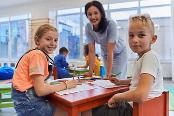 Image showing Creative kids during an art class in a daycare center or elementary school classroom drawing with female teacher.