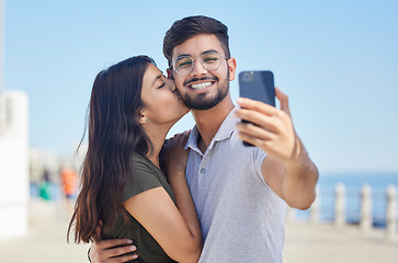 Image showing Phone, kiss or couple love taking a selfie on a romantic honeymoon, beach holiday or vacation in a summer romance. Smile, profile pictures or happy man enjoys quality bonding time with Indian partner