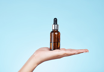 Image showing Hand, product and serum with a woman in studio on a blue background to promote an antiaging treatment. Skincare, beauty and bottle with a female model holding a container for cosmetic advertising