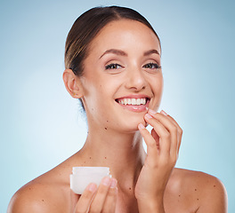 Image showing Portrait, skincare or lotion with a model woman holding a container in studio on blue background to promote beauty. Face, wellness or luxury and an attractive young female with cream to apply on skin