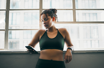 Image showing Idea, phone and exercise with a sports woman by a window, standing in the gym during a fitnesss workout. Health, thinking and a female athlete using social media or an app to track her training