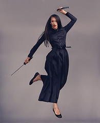 Image showing Ninja, swords and woman samurai in a studio jumping for a martial arts or assassin fighter skill. Fantasy, cosplay and female model in a warrior costume with blade isolated by a gray background.