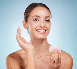 Image showing Portrait, beauty and skincare product with a model woman holding a container in studio on a blue background. Face, wellness or luxury and an attractive young female with cream to apply on skin